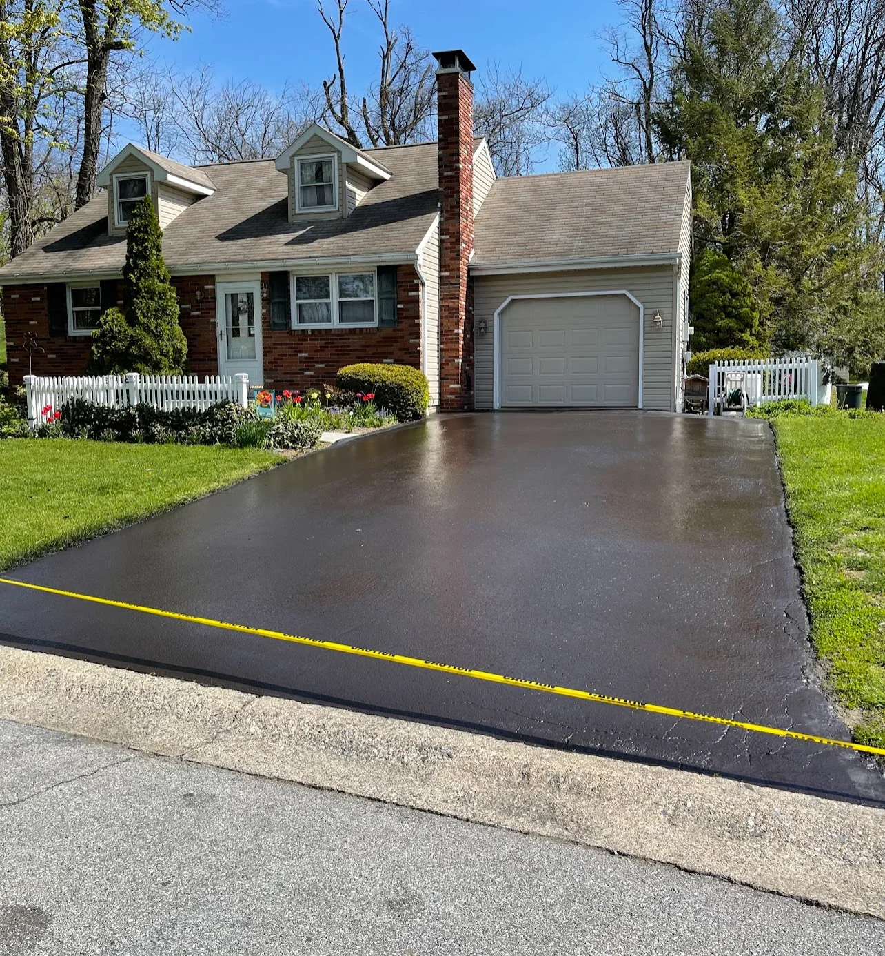 Newly sealed asphalt driveway with dark finish in front of brick home