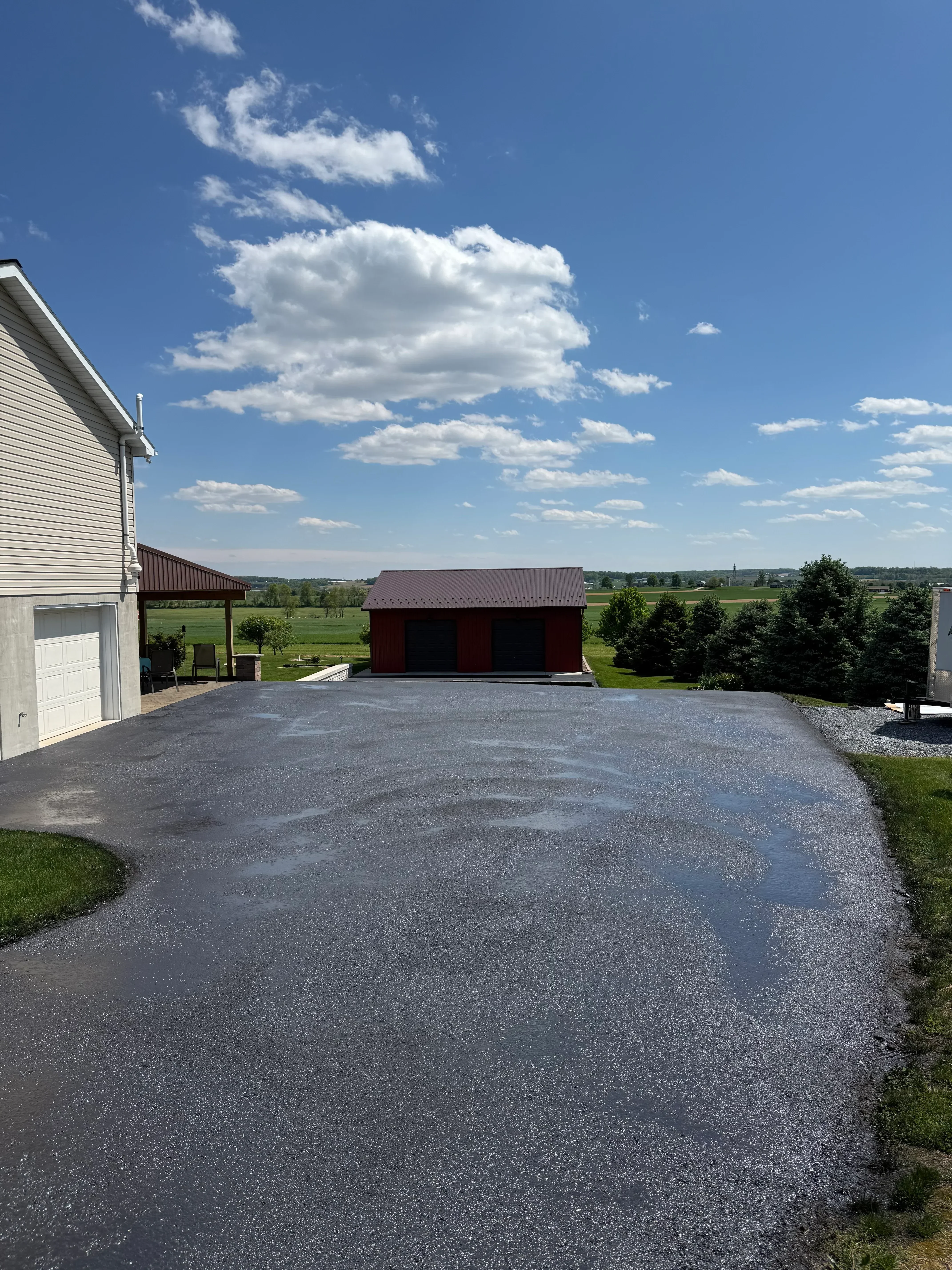 Newly sealed asphalt driveway with dark finish and clean edges adjacent to lawn