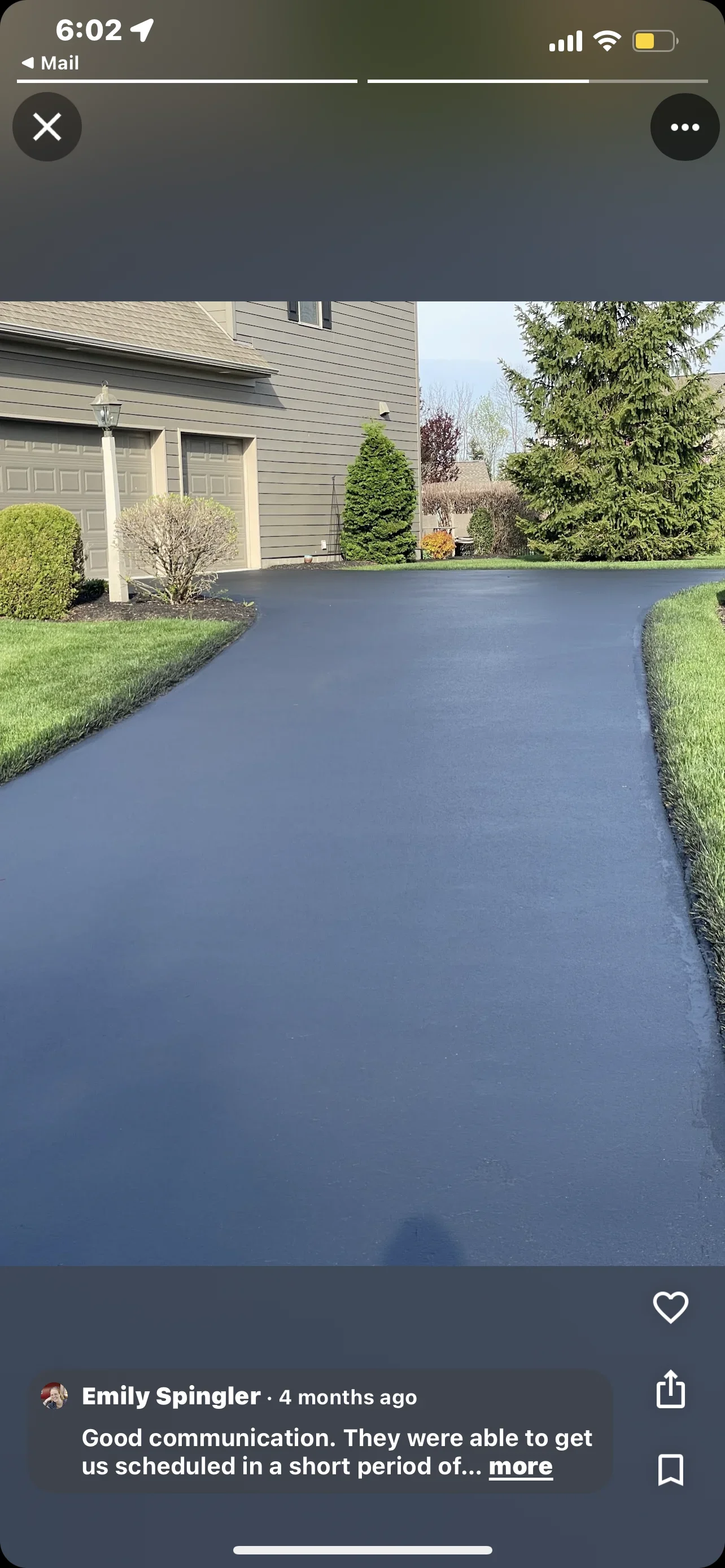 Newly sealed asphalt driveway with dark finish, bordered by green lawn and landscaping