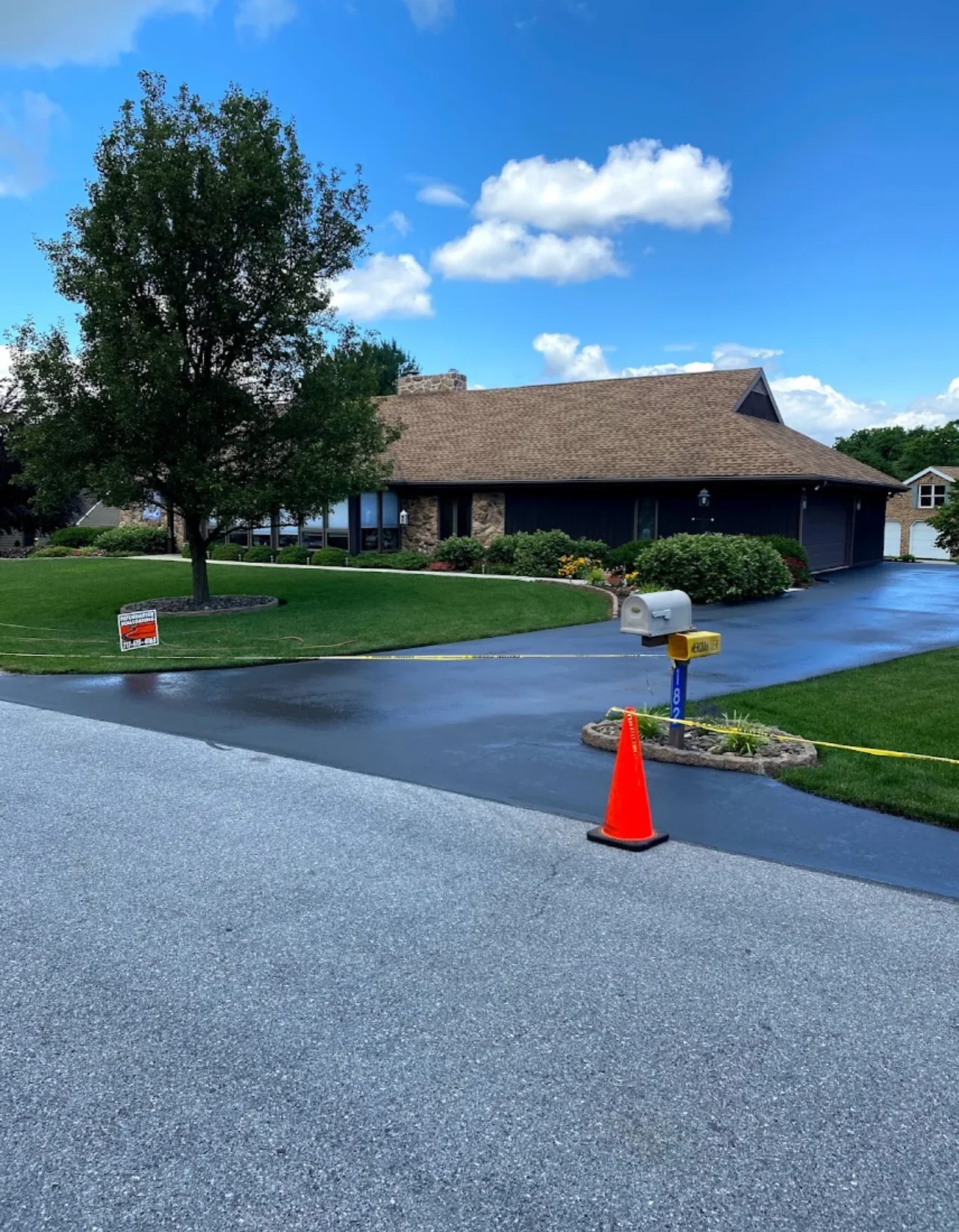 Newly sealed asphalt driveway with dark finish in front of brick home