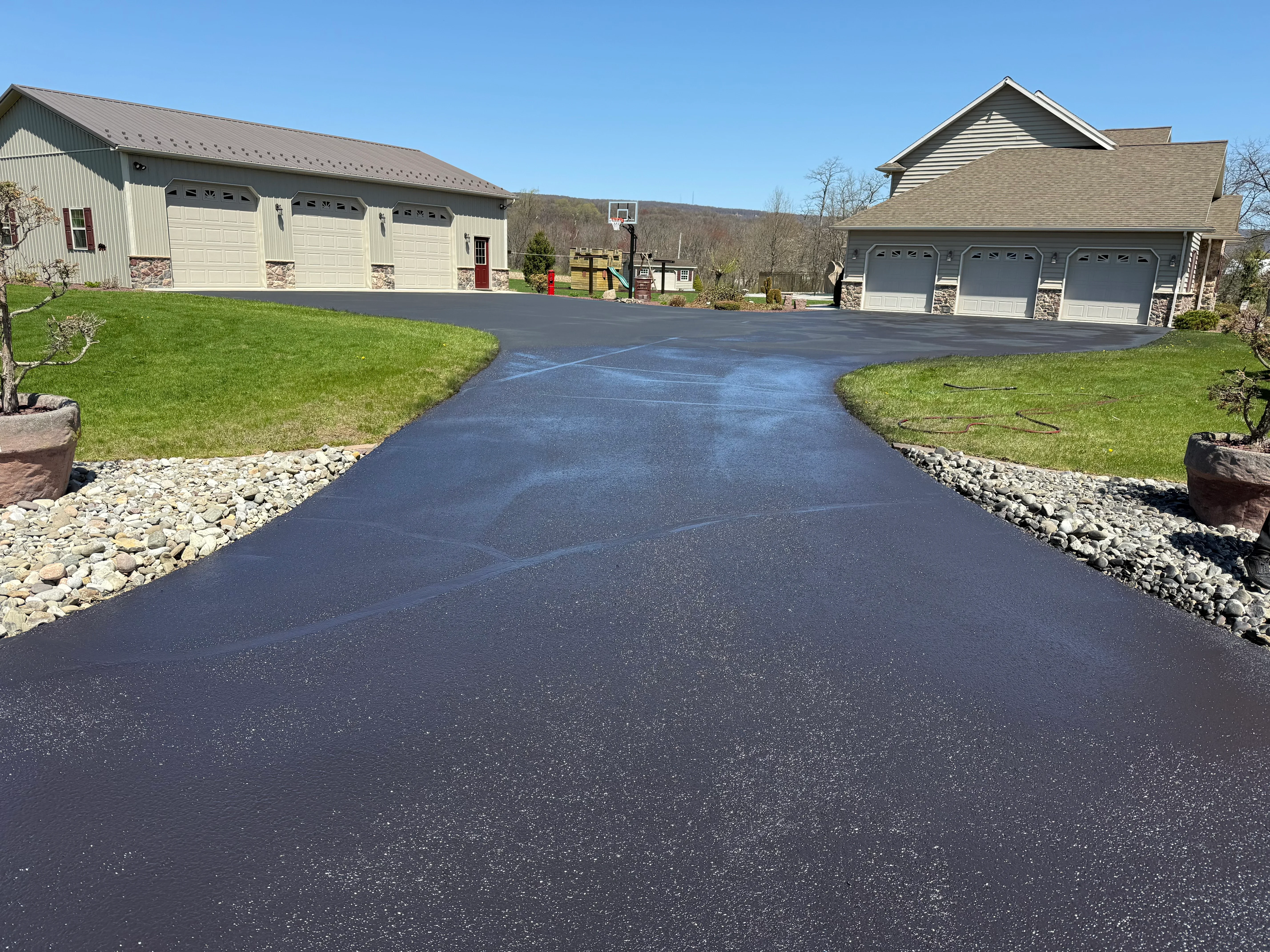 Newly sealed dark asphalt driveway with gravel borders and two residential garages