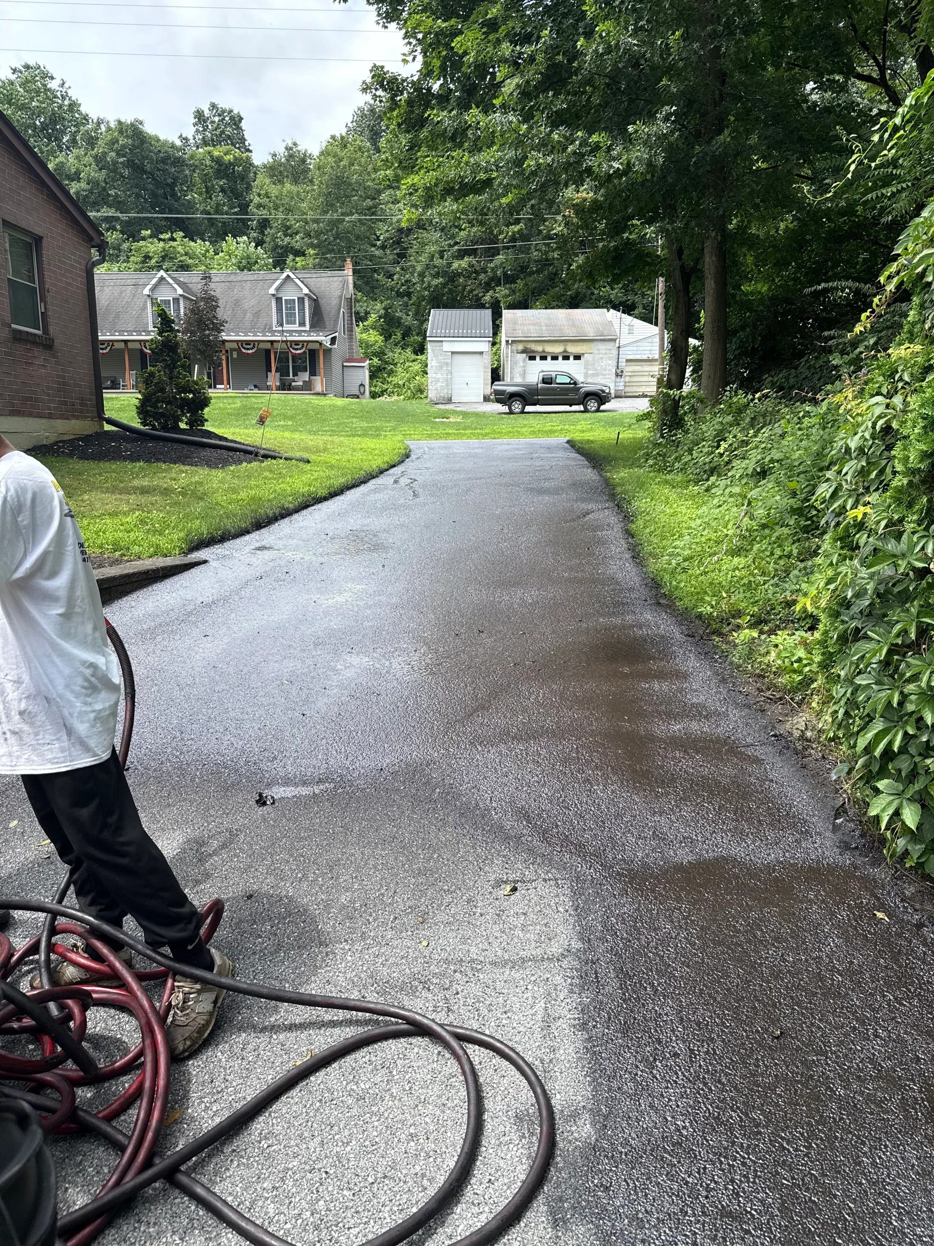 Sealed asphalt driveway with protective coating applied, showing dark finished surface next to green lawn
