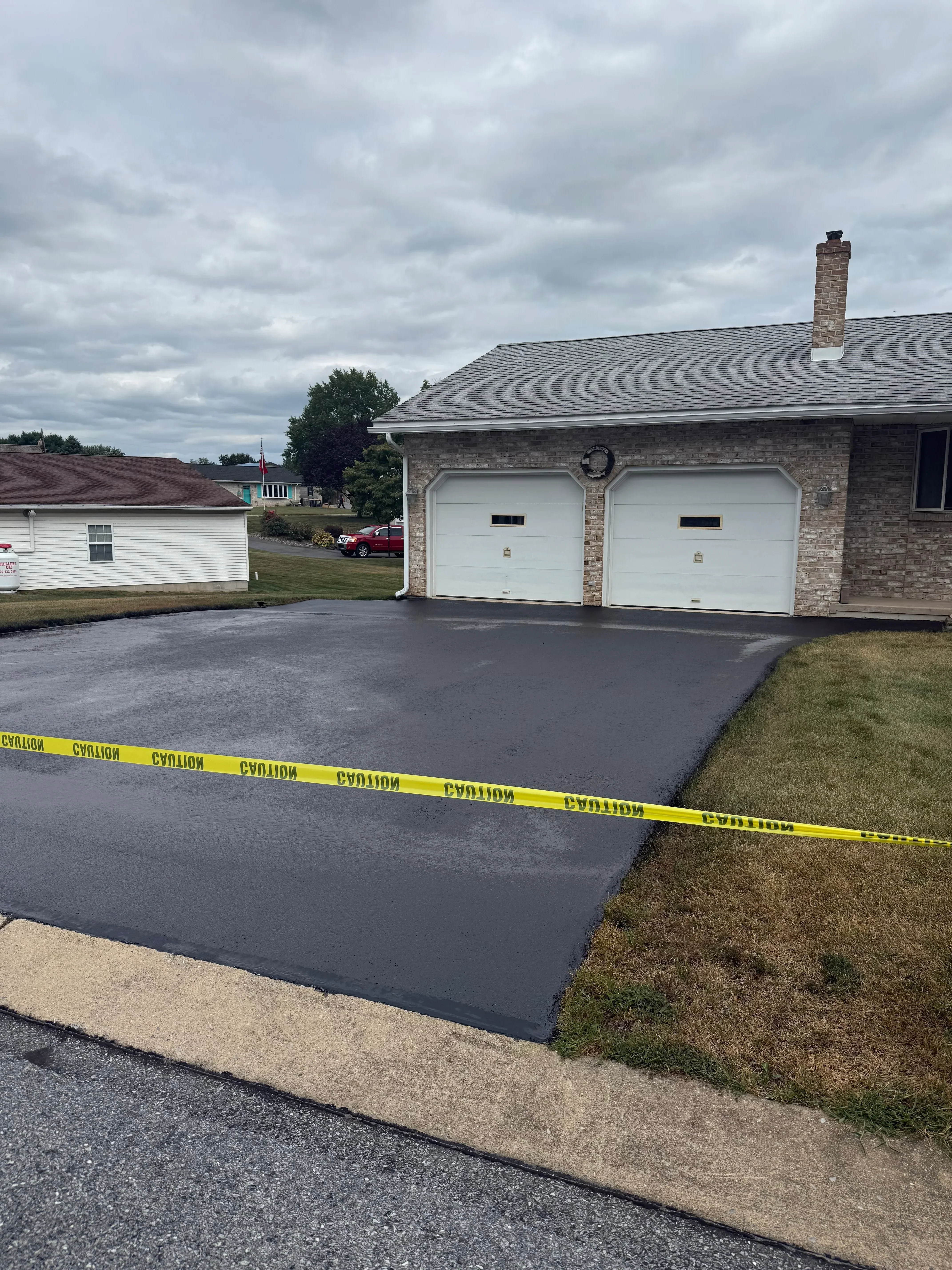 Newly seal-coated residential driveway with dark asphalt and concrete apron