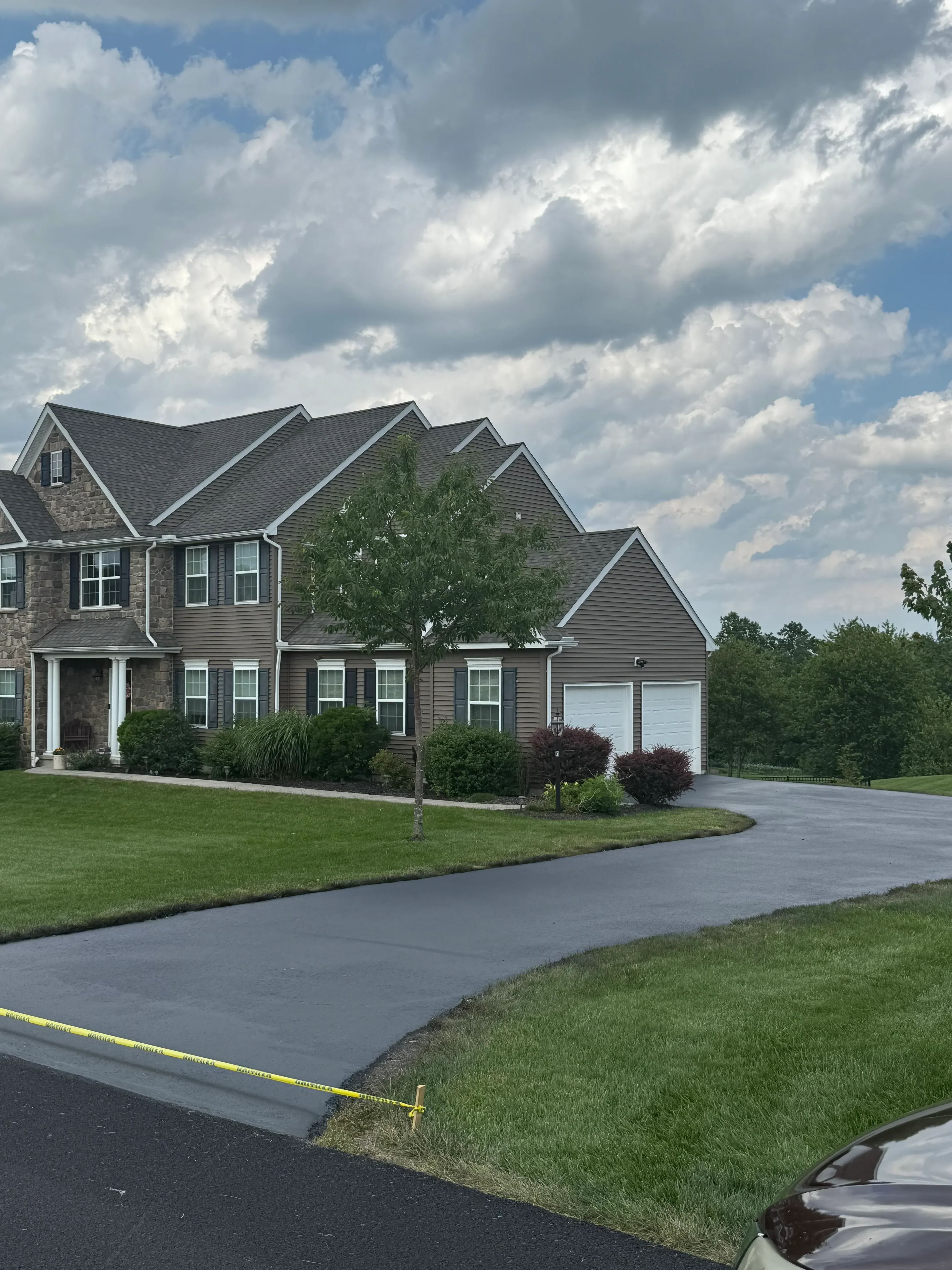 Newly paved asphalt driveway with clean edges alongside residential home and landscaping