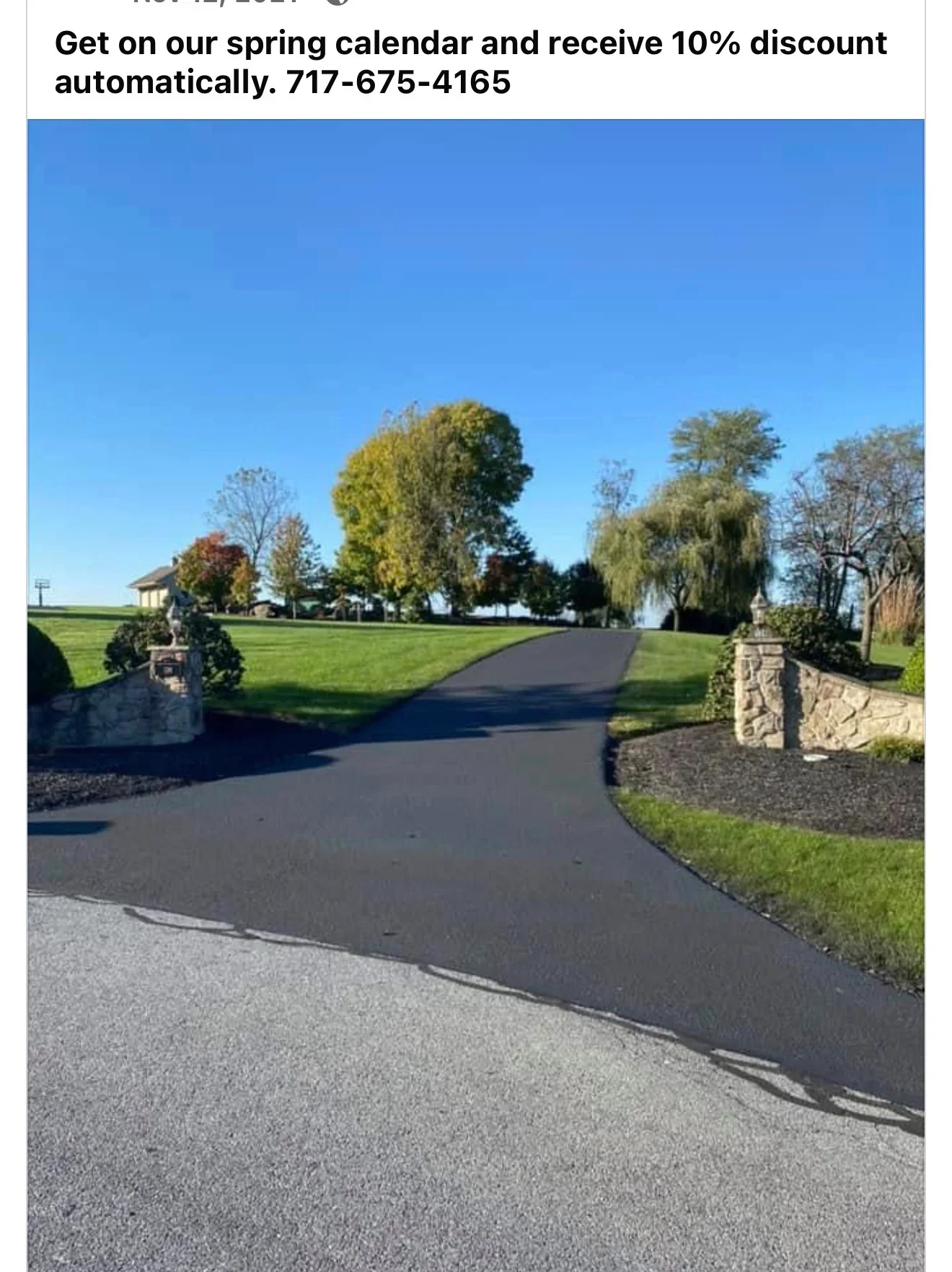 Curved asphalt driveway with stone entrance pillars and manicured lawn borders
