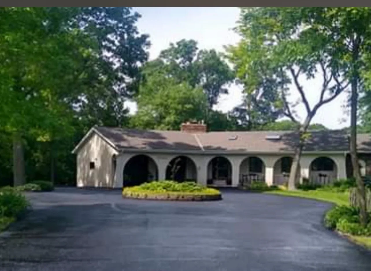 Sealed asphalt driveway with dark finish in front of white garage with arched openings