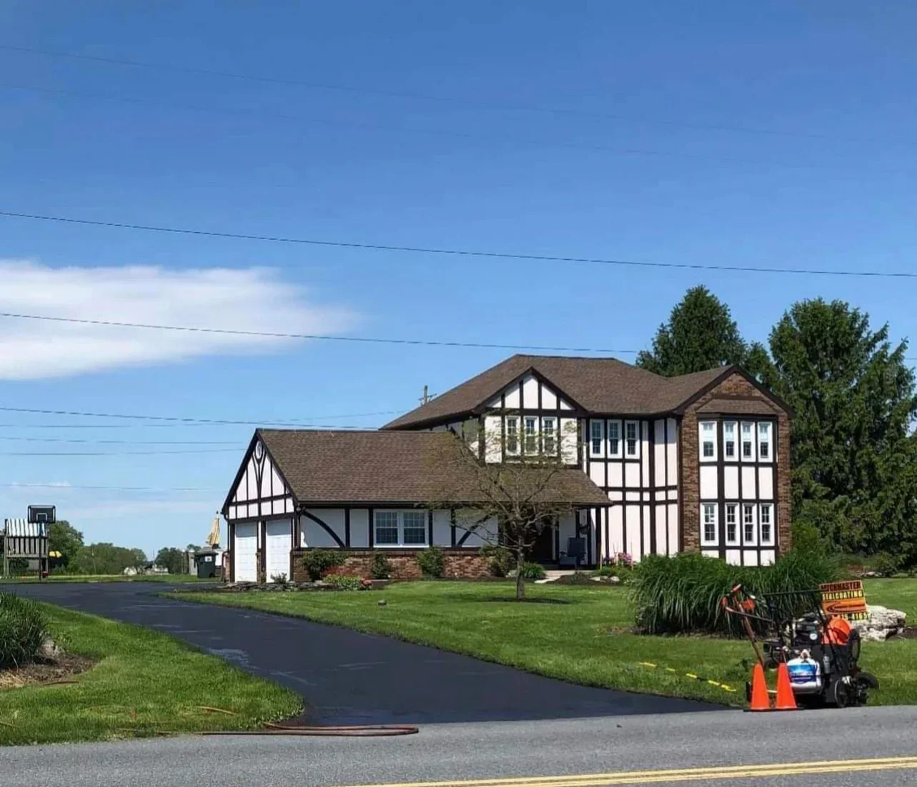 Freshly sealed asphalt driveway with dark finish in front of brick and white Tudor home