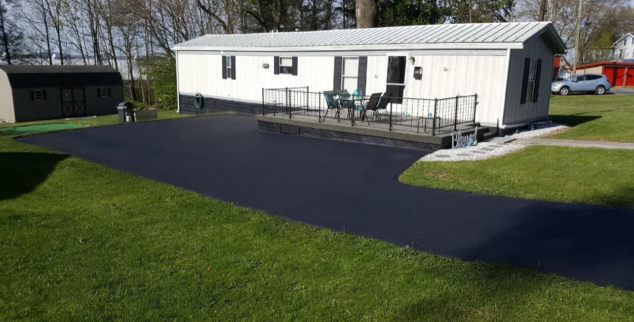 New black asphalt driveway with clean edges bordering green lawn at residential home