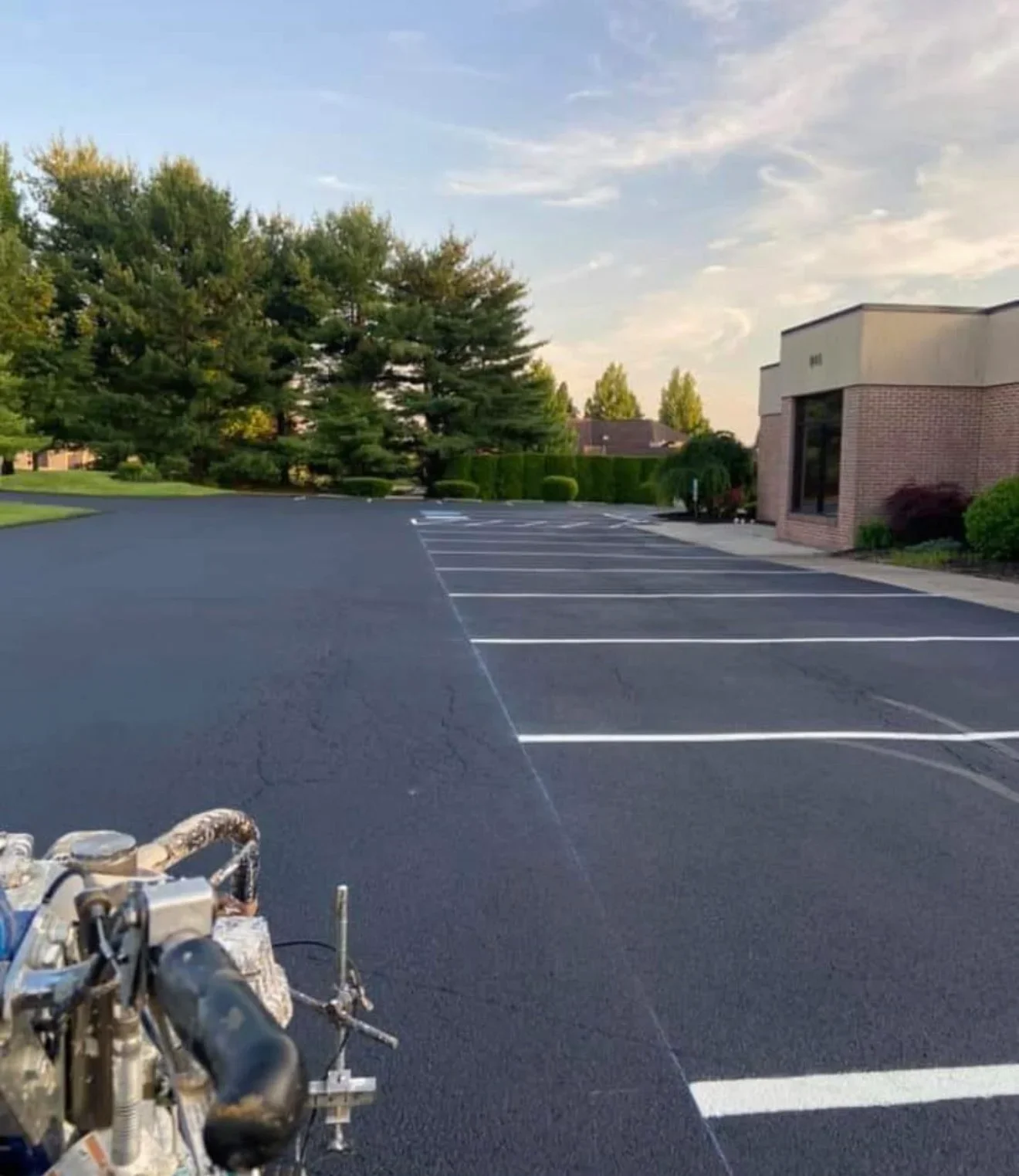 Sealed asphalt parking lot with white striped parking spaces and seal coating equipment