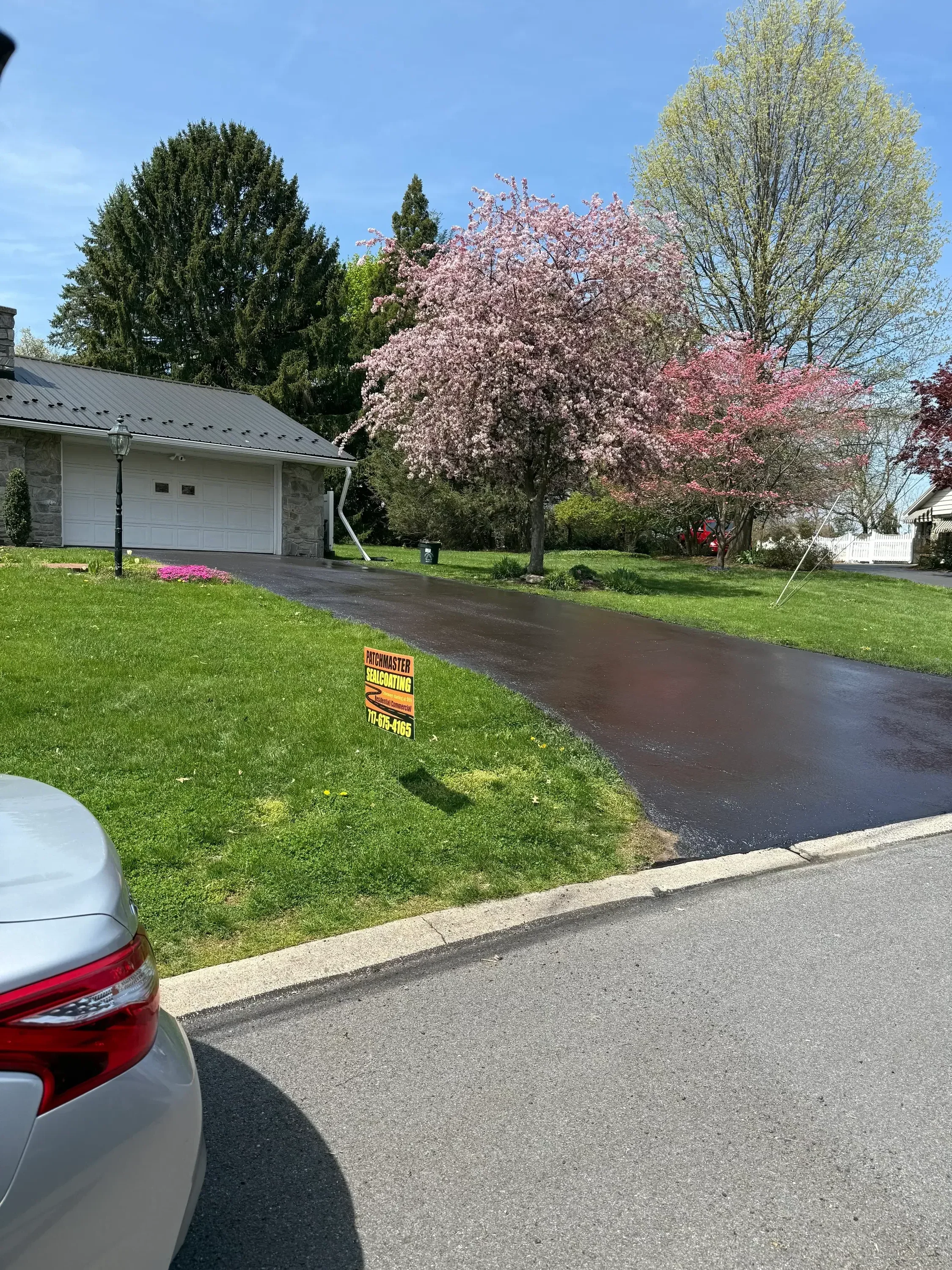Freshly seal-coated asphalt driveway with concrete curb and manicured lawn