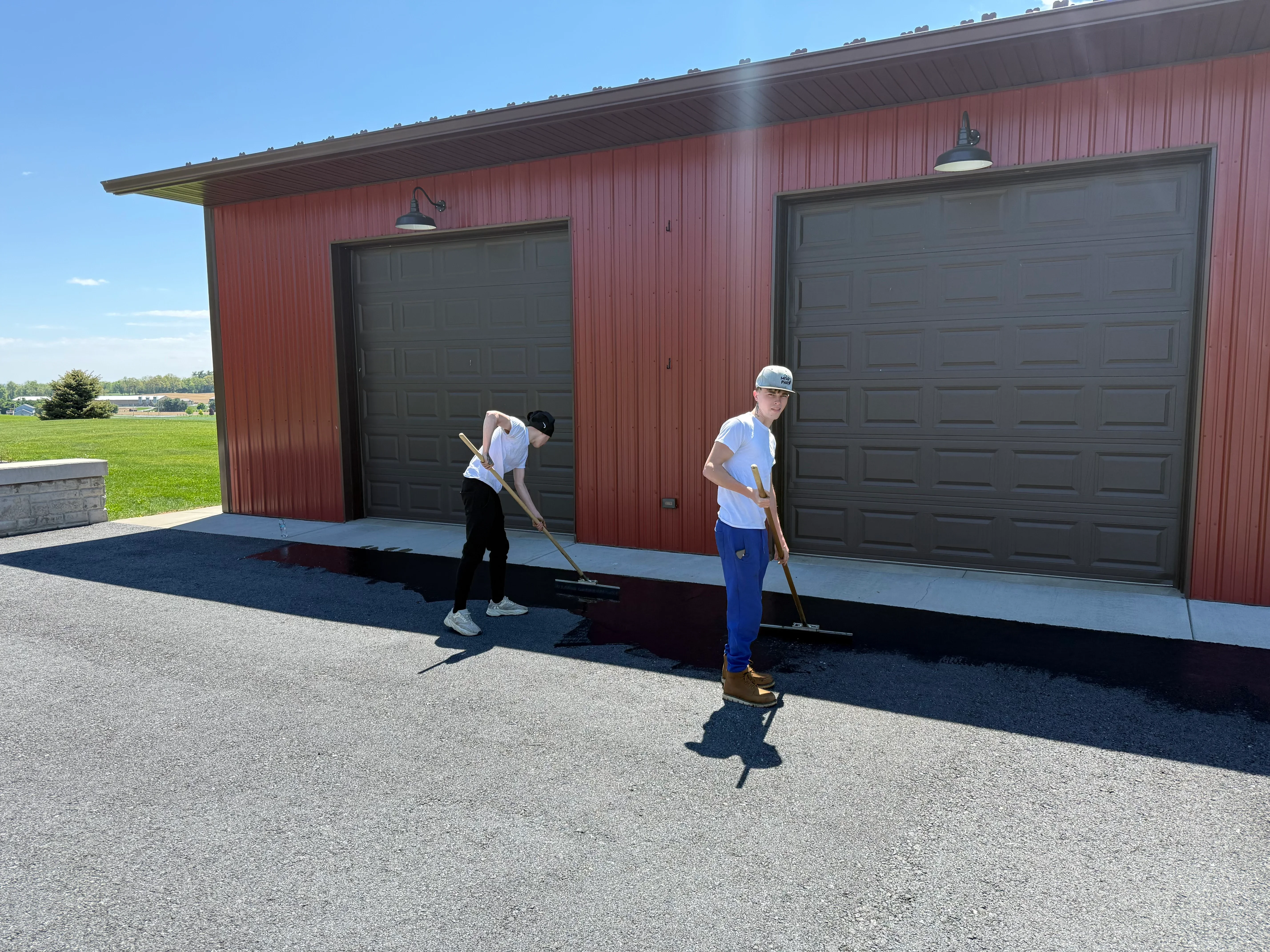 Seal coating application on asphalt driveway in front of red garage with black overhead doors