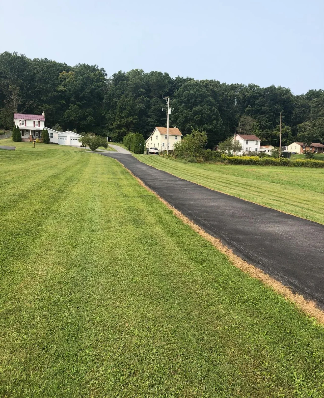 New black asphalt driveway with clean edges on residential property with manicured lawn