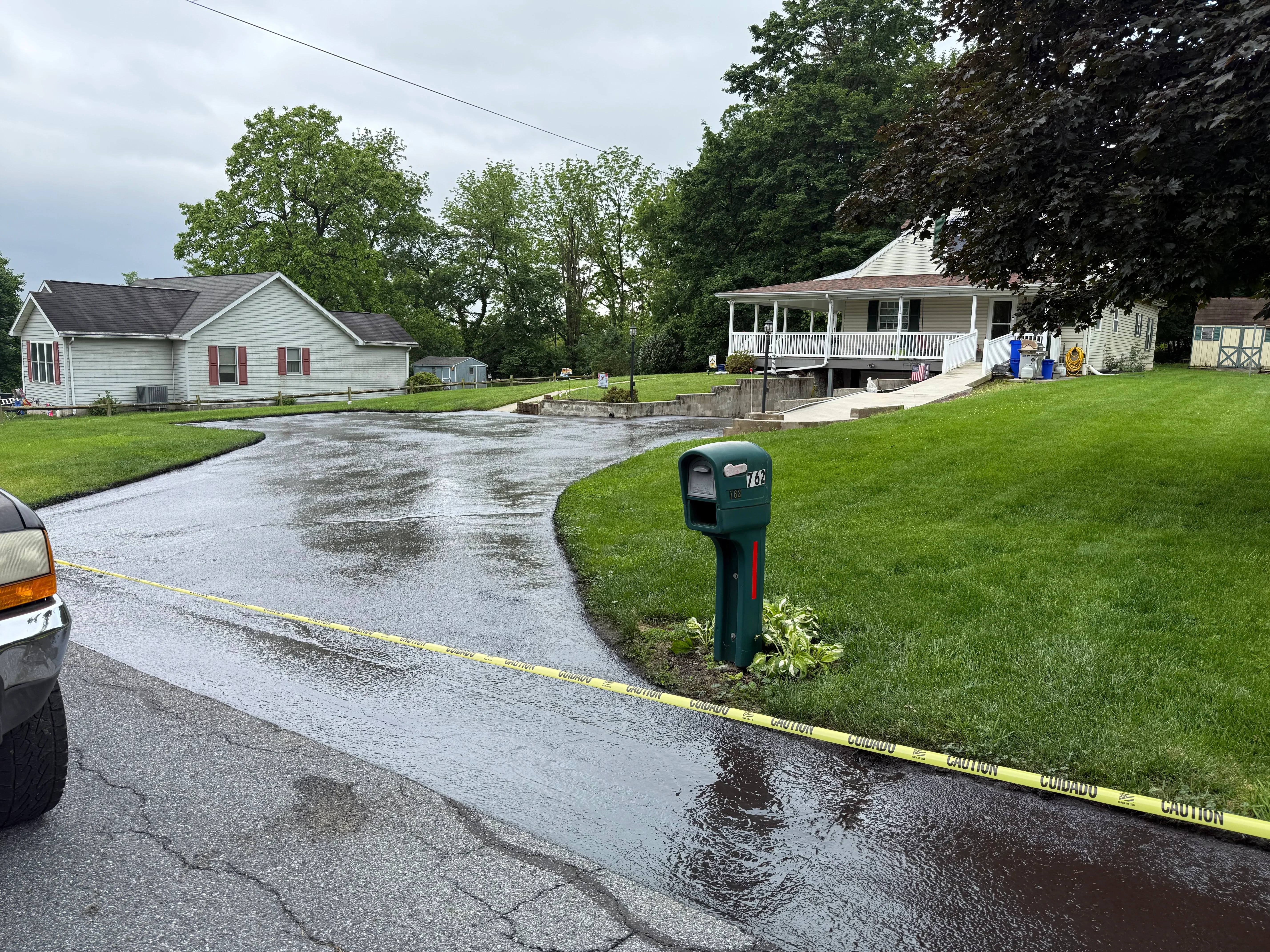 Wet asphalt driveway with patched sections and fresh seal coating application