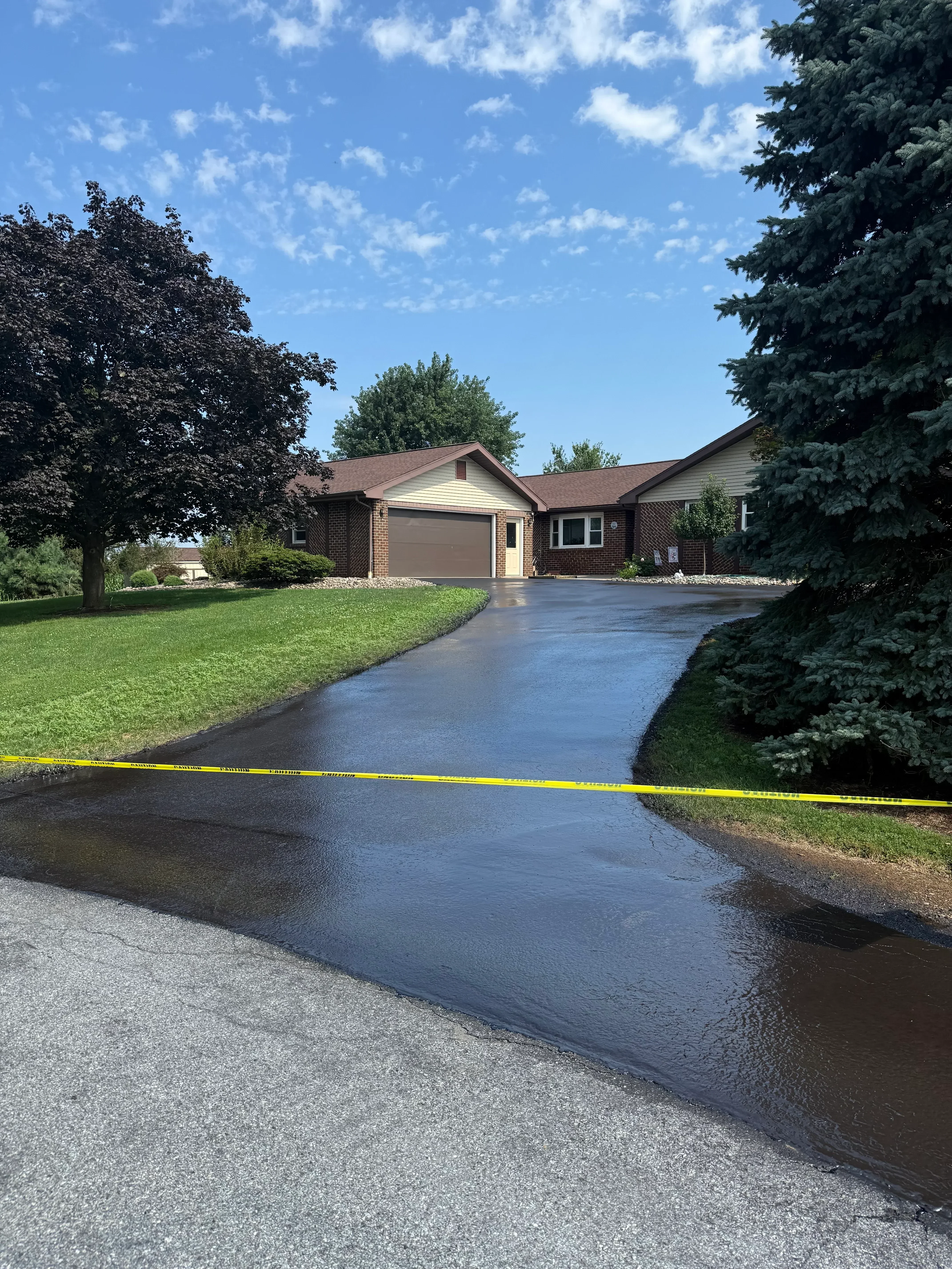 Newly sealed asphalt driveway with dark finish in front of brick residential home