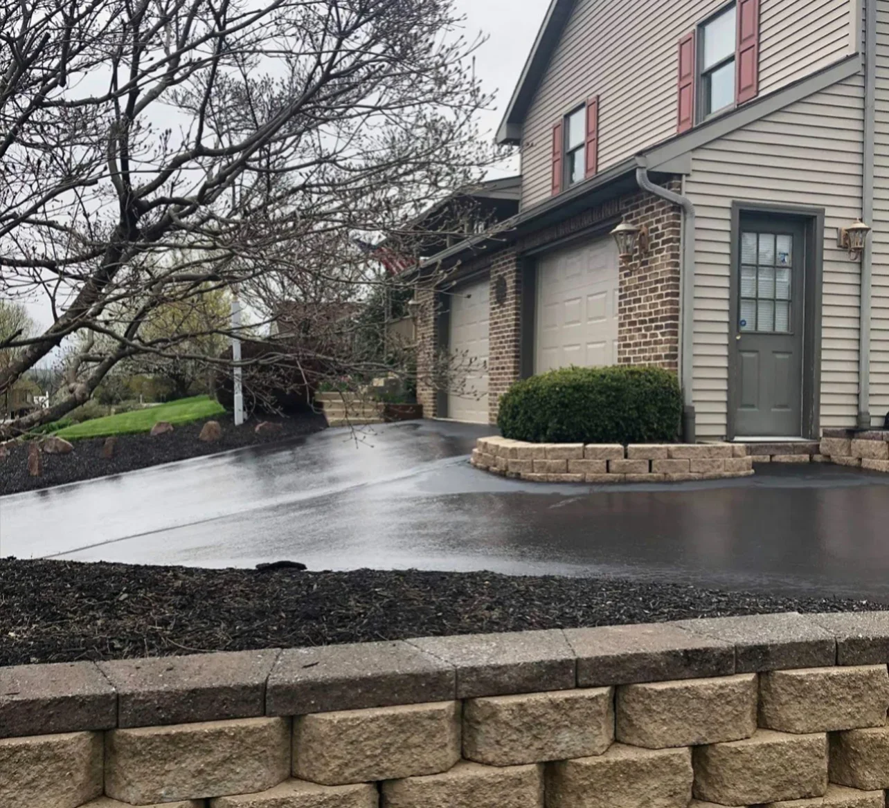 Sealed asphalt driveway with dark finish, brick retaining wall, and foundation planter